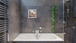 Bathroom of the Haidhausen period apartment with bathtub, rain shower, dark tiles, and hanging green plant