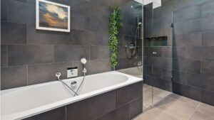 Modern bathroom with dark tiles, bathtub, and glass shower in an old building apartment in Haidhausen
