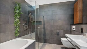 Modern bathroom in the Haidhausen old building apartment with walk-in glass shower, bathtub, and dark tiles