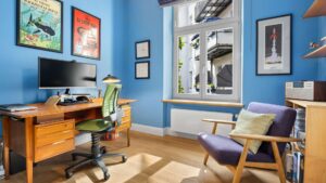 Study of the old building apartment in Haidhausen with blue walls, wooden desk, green office chair, and art prints