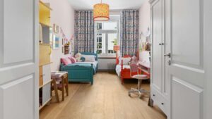 View from the hallway into a children's room with two colorful beds in an old-style apartment in Haidhausen