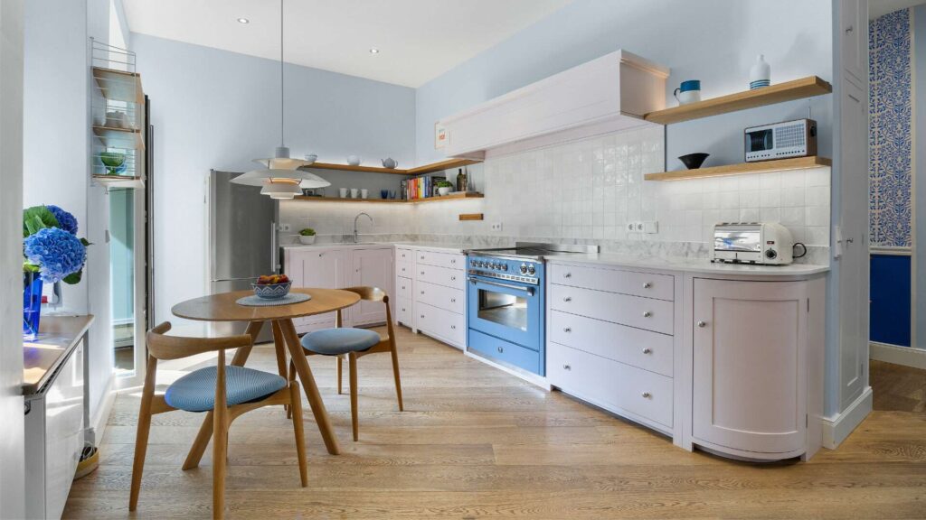 Küche der Altbauwohnung Haidhausen mit blauem Range-Ofen, rundem Holztisch und offenen Regalen