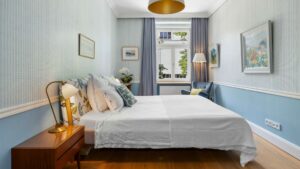 Bedroom of the Haidhausen old building apartment with blue wallpaper, upholstered bed and golden pendant light