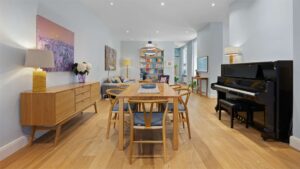 Dining area of the Haidhausen old building apartment with wooden table, sideboard, bookshelf, and black piano