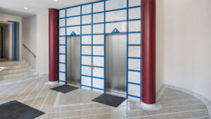 Two elevator doors between red columns and a mosaic wall in the entrance area of an apartment building in Munich-Haidhausen