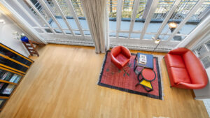 Bird's-eye view from the gallery of a loft living room with a red sofa, armchair, and bookshelf in Haidhausen