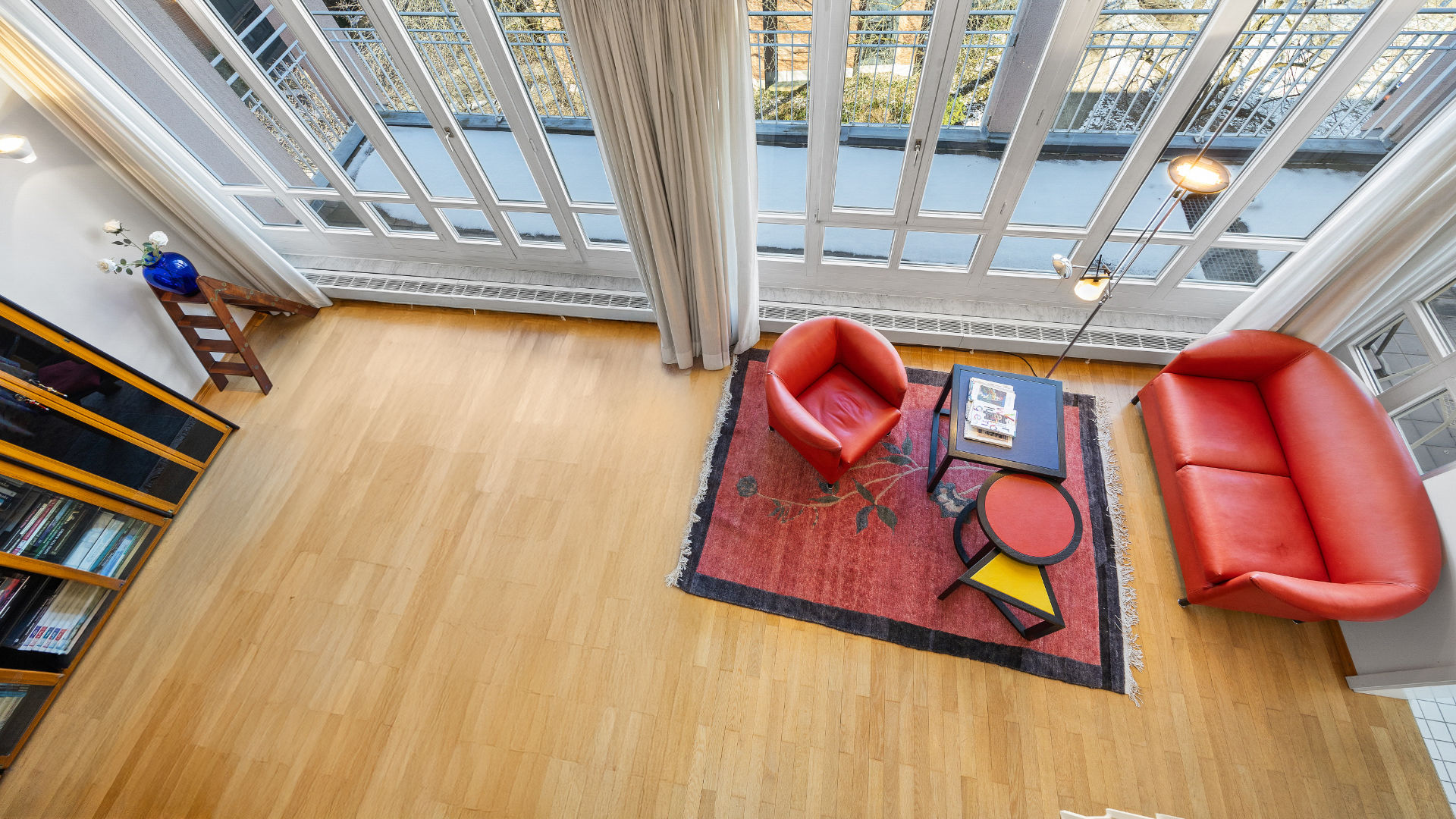 Bird's-eye view from the gallery of a loft living room with a red sofa, armchair, and bookshelf in Haidhausen