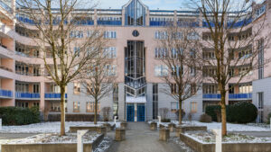 Modern residential complex with a symmetrical glass facade and an avenue of trees in front of the entrance in Munich-Haidhausen