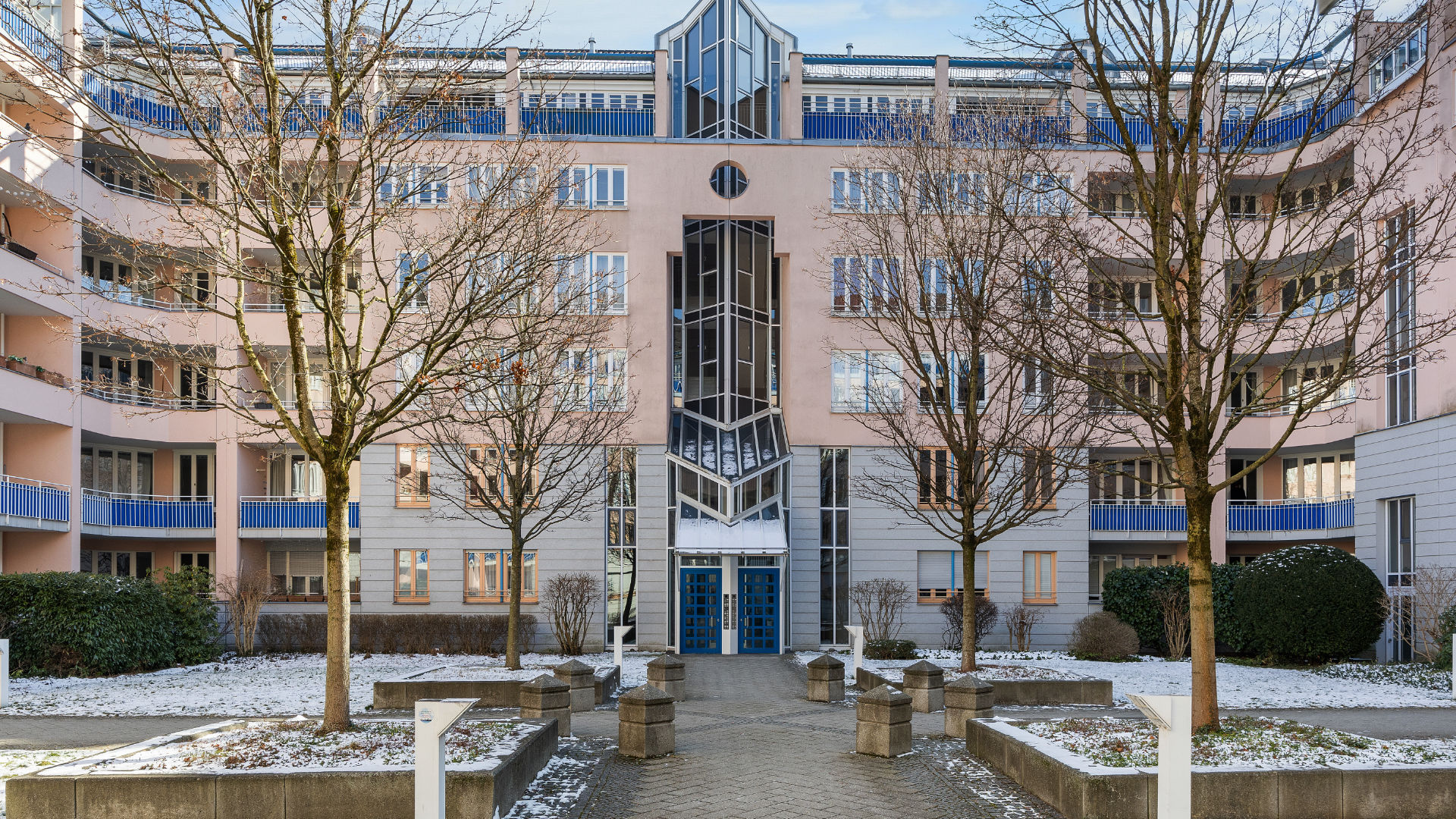 Modern residential complex with a symmetrical glass facade and an avenue of trees in front of the entrance in Munich-Haidhausen