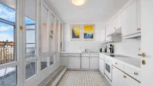 Narrow white kitchen with tiled floor, yellow wall art and access to the glazed balcony in Haidhausen
