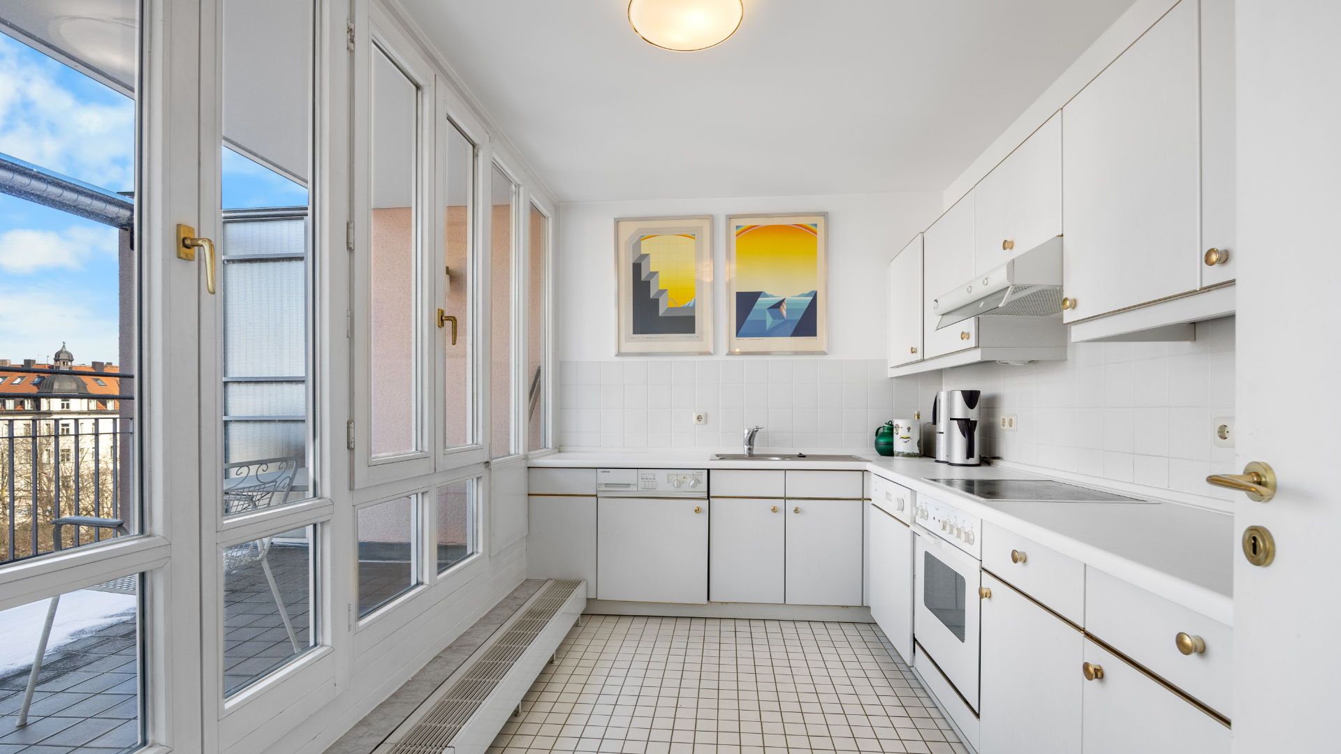 Narrow white kitchen with tiled floor, yellow wall art and access to the glazed balcony in Haidhausen