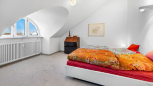 Bedroom with round window in sloped ceiling, bed with orange bedspread in Munich-Haidhausen apartment