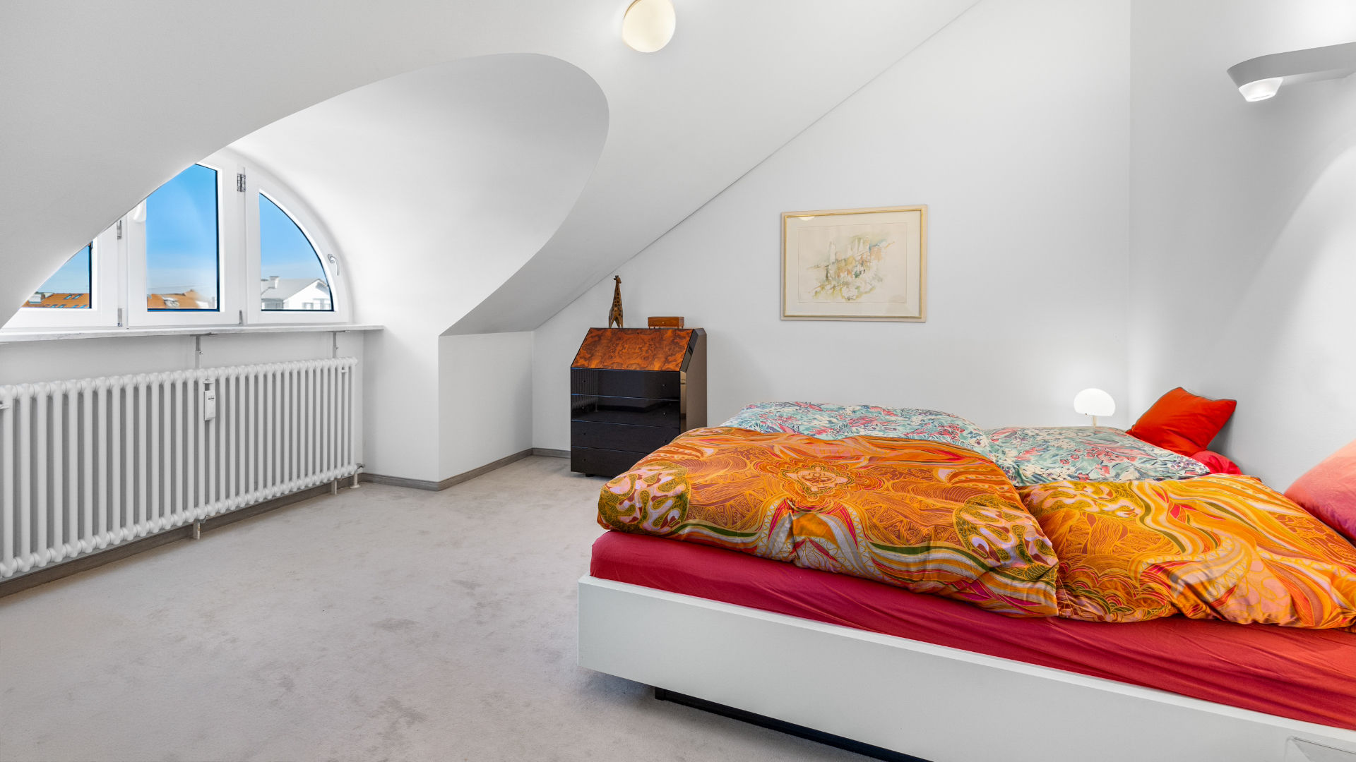 Bedroom with round window in sloped ceiling, bed with orange bedspread in Munich-Haidhausen apartment