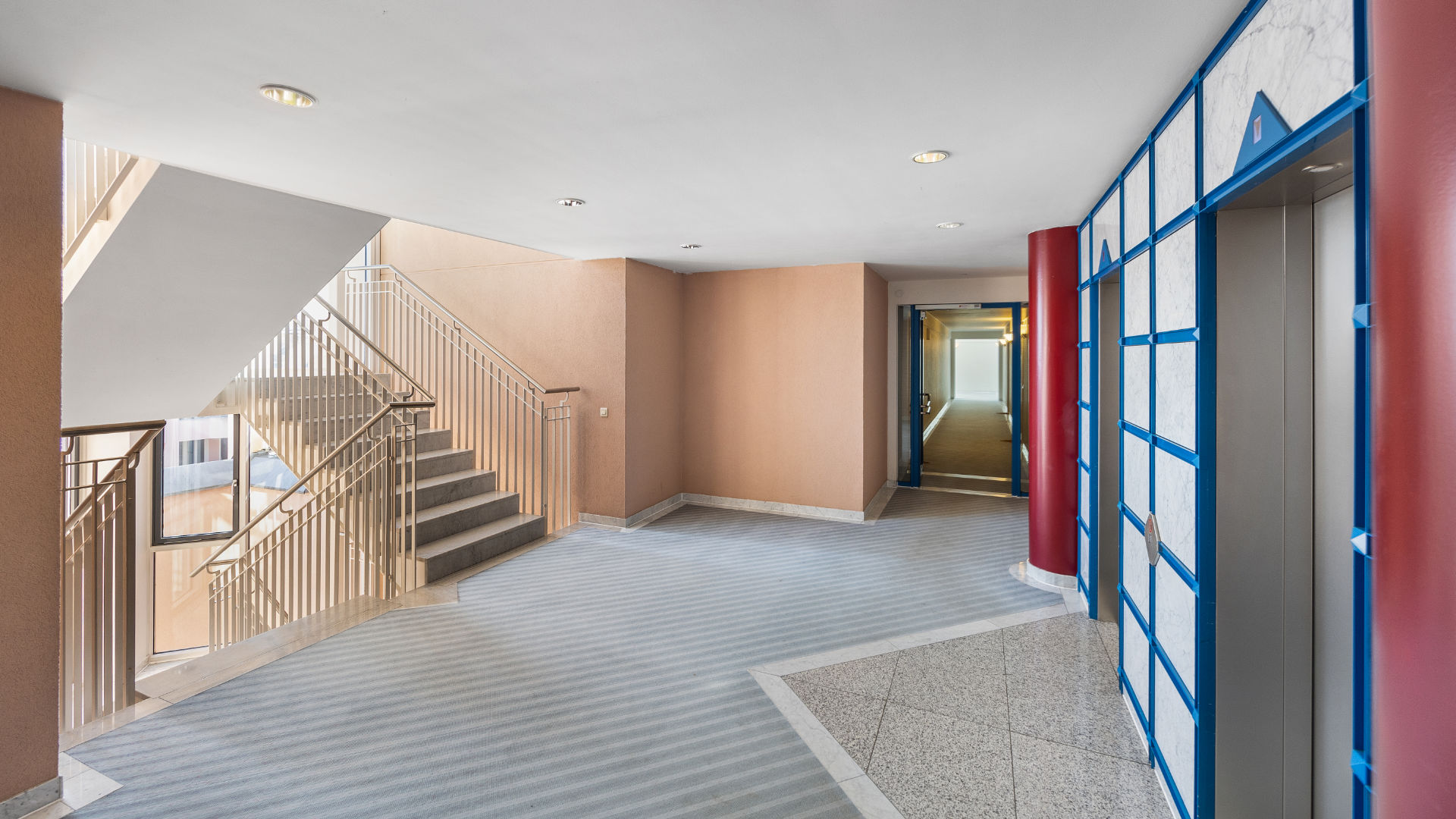 Stairwell with elevator, blue-framed door, and carpeted flooring in an apartment building in Munich-Haidhausen