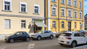 Yellow-beige old building facade with a small shop and parked cars in Munich-Haidhausen