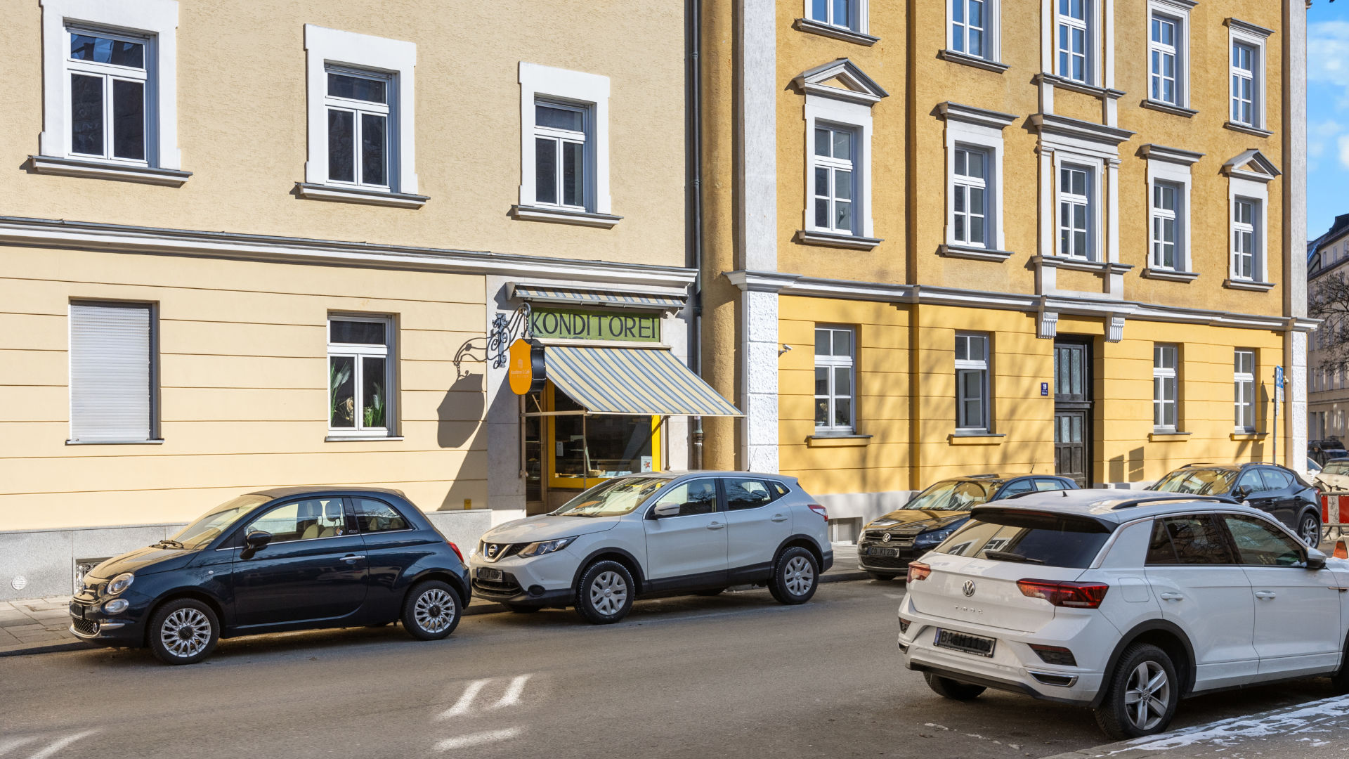 Yellow-beige old building facade with a small shop and parked cars in Munich-Haidhausen