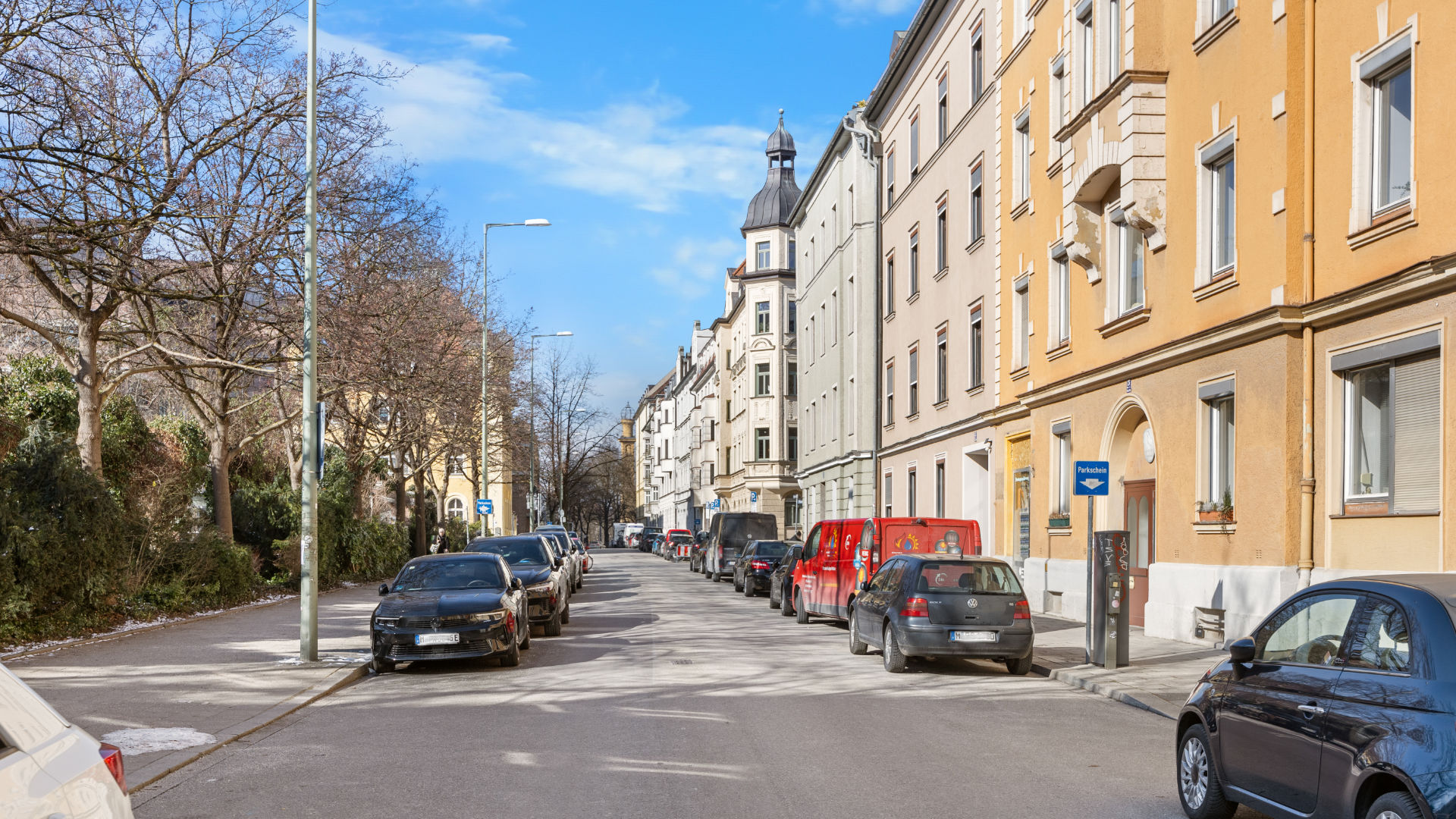 Tree-lined residential street with a yellow facade and parked cars in Munich-Haidhausen under a blue sky