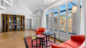 Loft-style living room with a sloped ceiling, glass-fronted bookcase, and red leather armchairs in a Munich-Haidhausen condominium