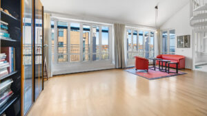 Loft-like living room with red vintage armchair, bookshelf, and large windows in a Munich-Haidhausen apartment