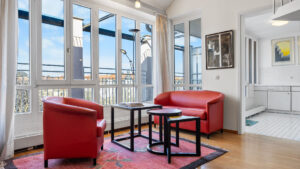 Two red leather armchairs in front of a window, white gallery staircase in the background in a Munich-Haidhausen loft apartment