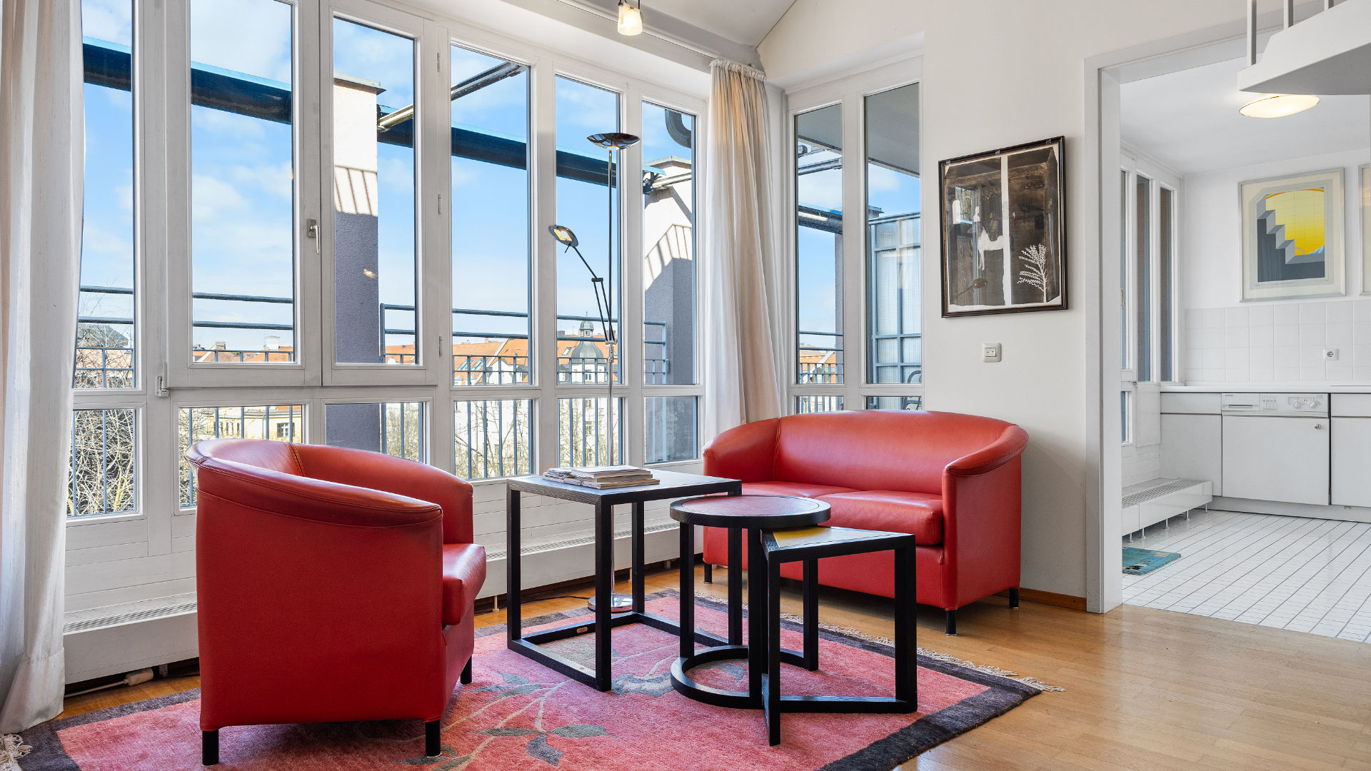 Two red leather armchairs in front of a window, white gallery staircase in the background in a Munich-Haidhausen loft apartment