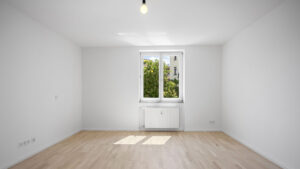 Empty bright room with a window, radiator, and wooden floor in a rented apartment in Munich-Isarvorstadt