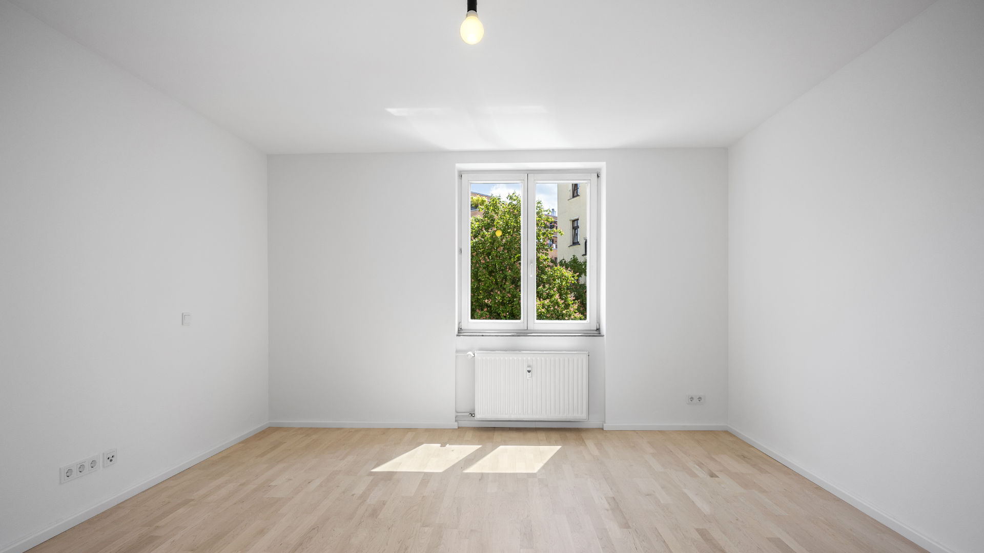 Empty bright room with a window, radiator, and wooden floor in a rented apartment in Munich-Isarvorstadt