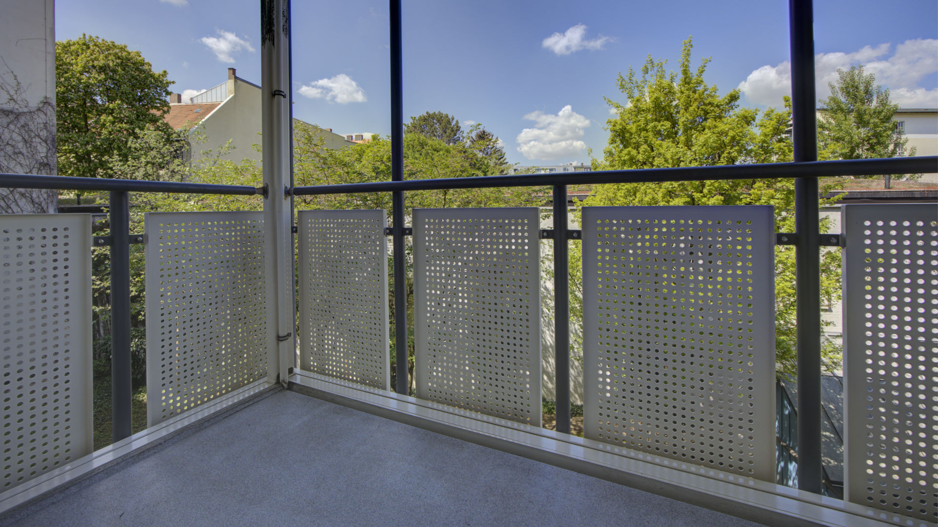Balcony with perforated metal privacy screen and view of rooftops in Isarvorstadt