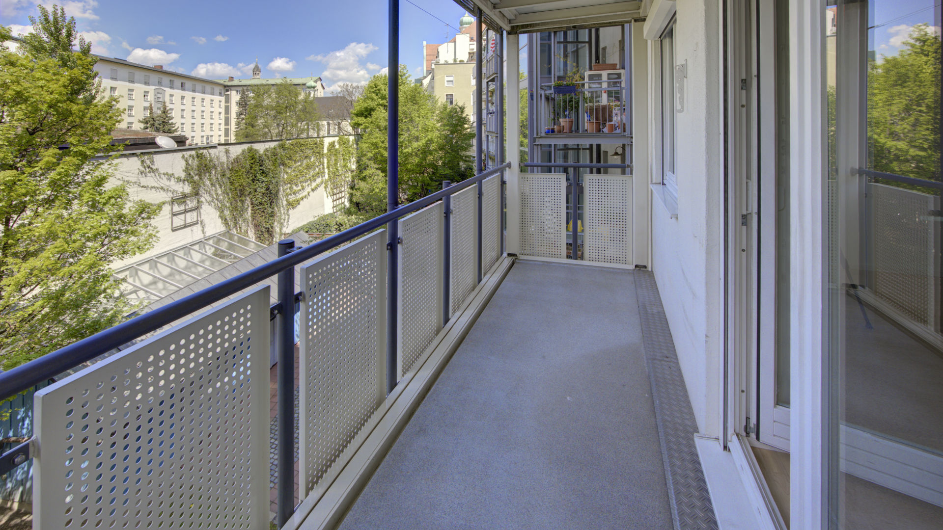 Long balcony with metal railing and view of residential buildings and trees in a rental apartment in Munich-Isarvorstadt