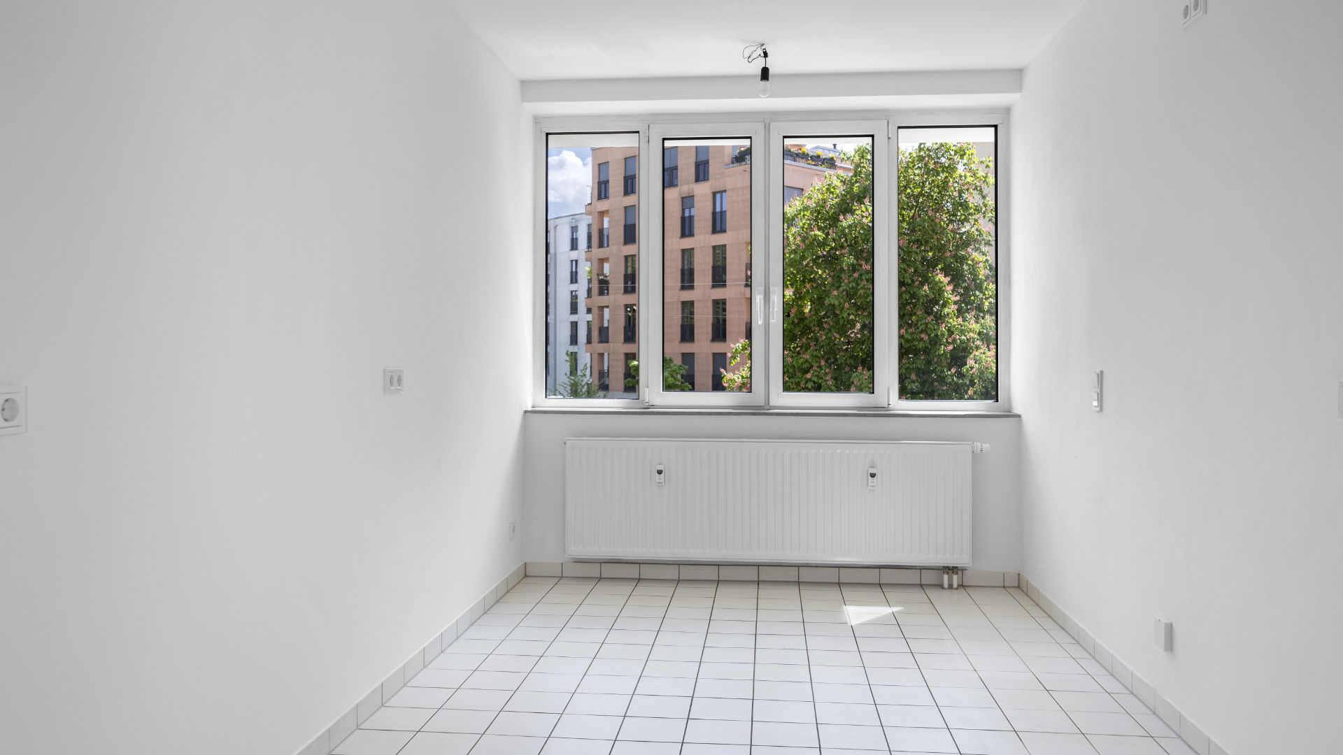 Empty kitchen with tile floor and window overlooking trees in an apartment for rent in Munich Isarvorstadt