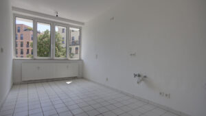 Empty kitchen with tiled floor, three windows, and a view of old buildings in a Munich Isarvorstadt rental apartment