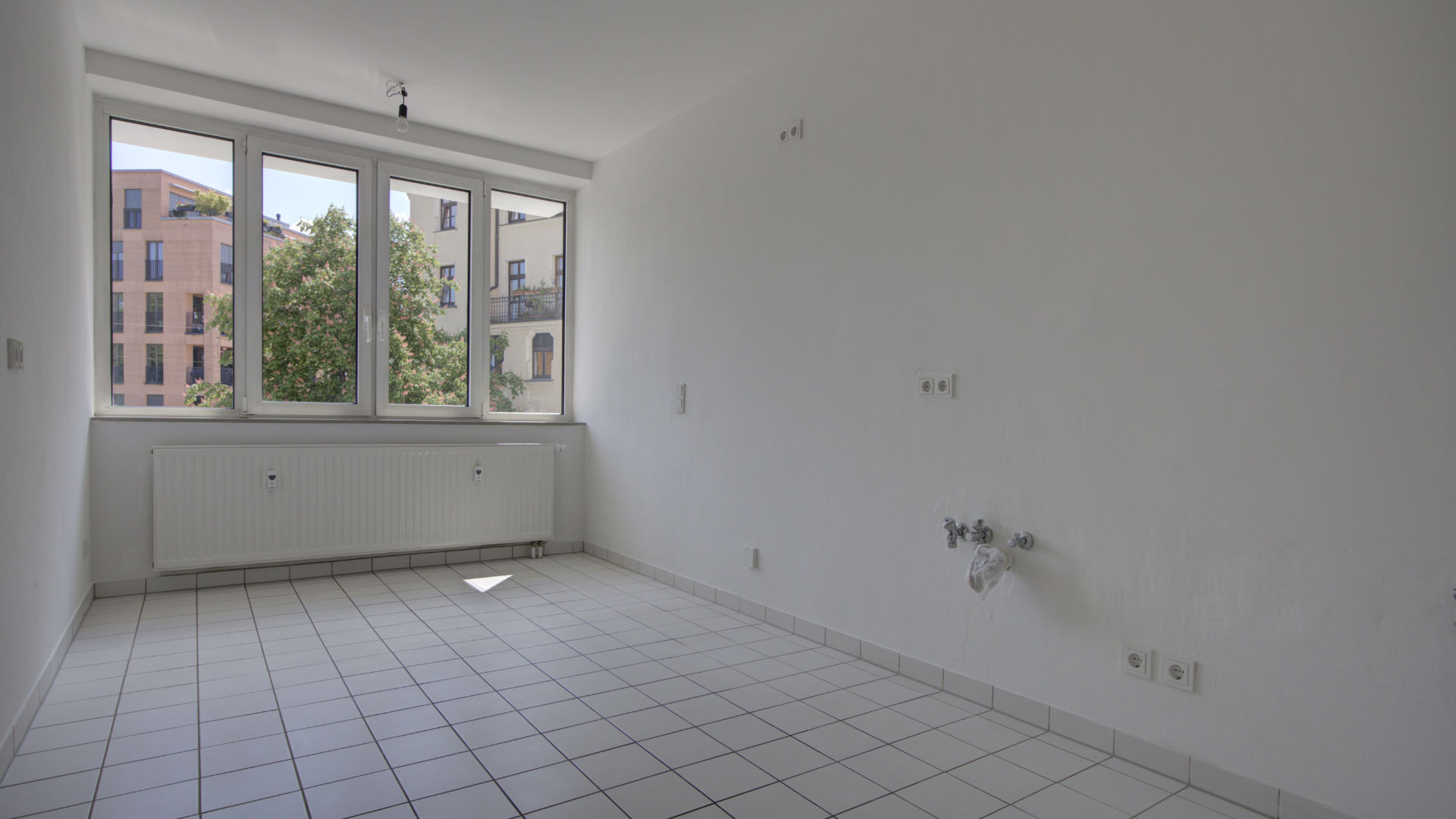 Empty kitchen with tiled floor, three windows, and a view of old buildings in a Munich Isarvorstadt rental apartment