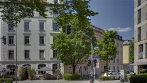 Busy intersection with bright old building facades and trees in Munich's Isarvorstadt district in sunny weather