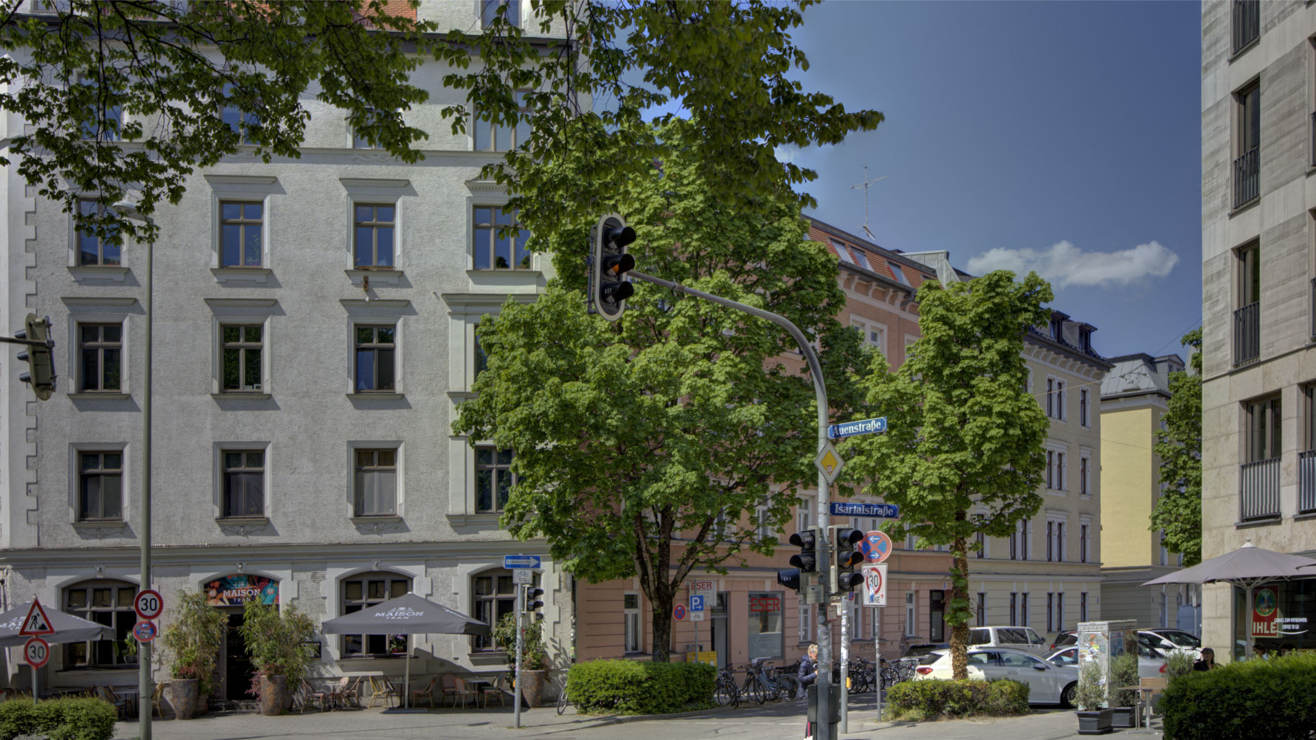 Busy intersection with bright old building facades and trees in Munich's Isarvorstadt district in sunny weather