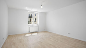 Empty room with window, radiator, and light parquet flooring in Munich-Isarvorstadt apartment