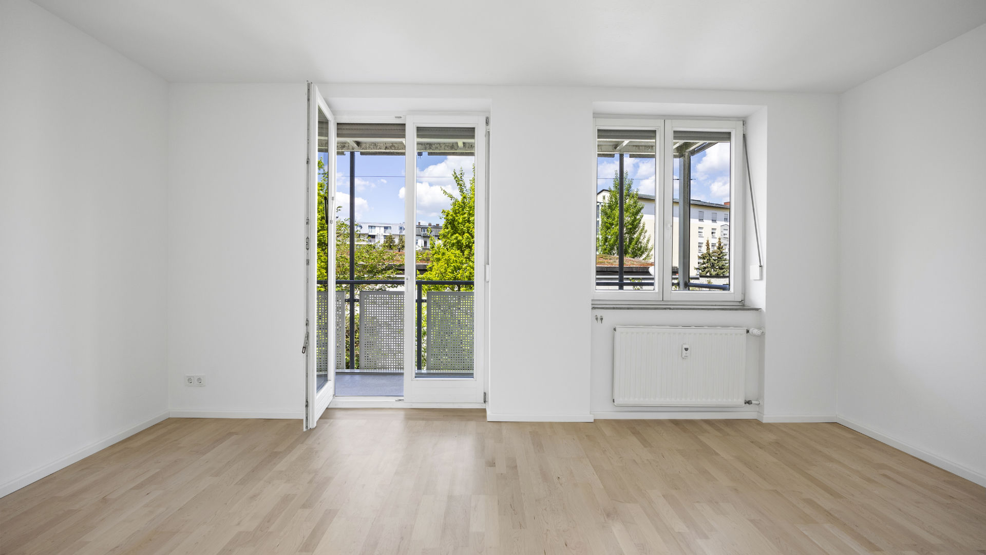 Empty room with balcony access, two windows, and a green view in a shared apartment in Munich-Isarvorstadt