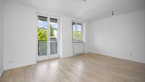 Empty room with two windows, radiator, and light parquet flooring in rental apartment in Munich Isarvorstadt