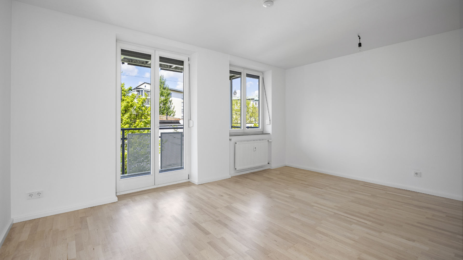 Empty room with two windows, radiator, and light parquet flooring in rental apartment in Munich Isarvorstadt