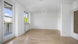 Empty room with balcony door, radiator, and light parquet flooring in a rental apartment in Munich-Isarvorstadt