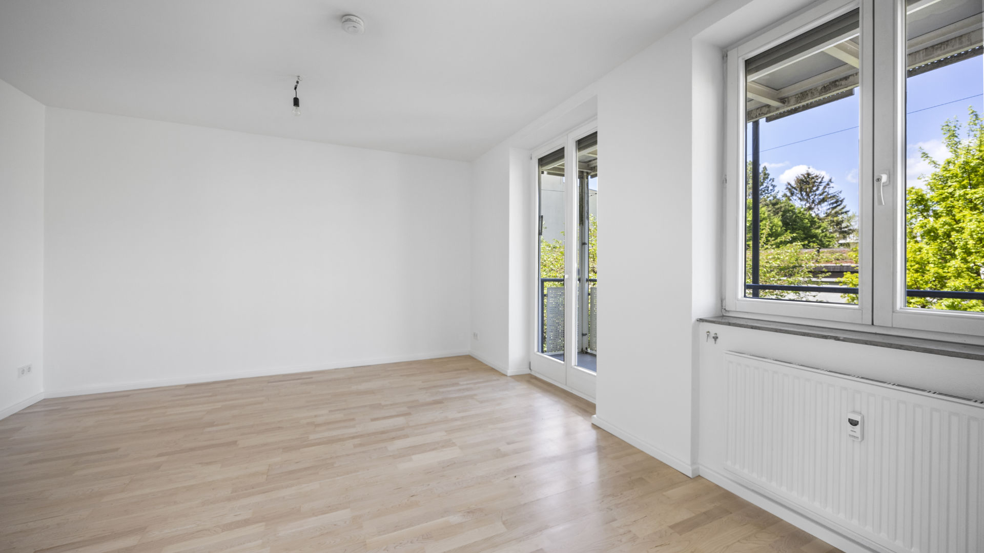 Empty bright room with large window and light parquet flooring in apartment for rent Munich-Isarvorstadt