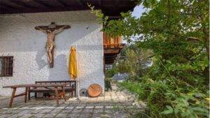 Gepflasterte Terrasse mit Kruzifix an der Fassade und Sitzbank des Hauses in Kochel am See