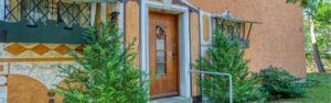 Entrance area of a house in Laim with a terracotta-colored facade, wooden door, and decorative shutters.