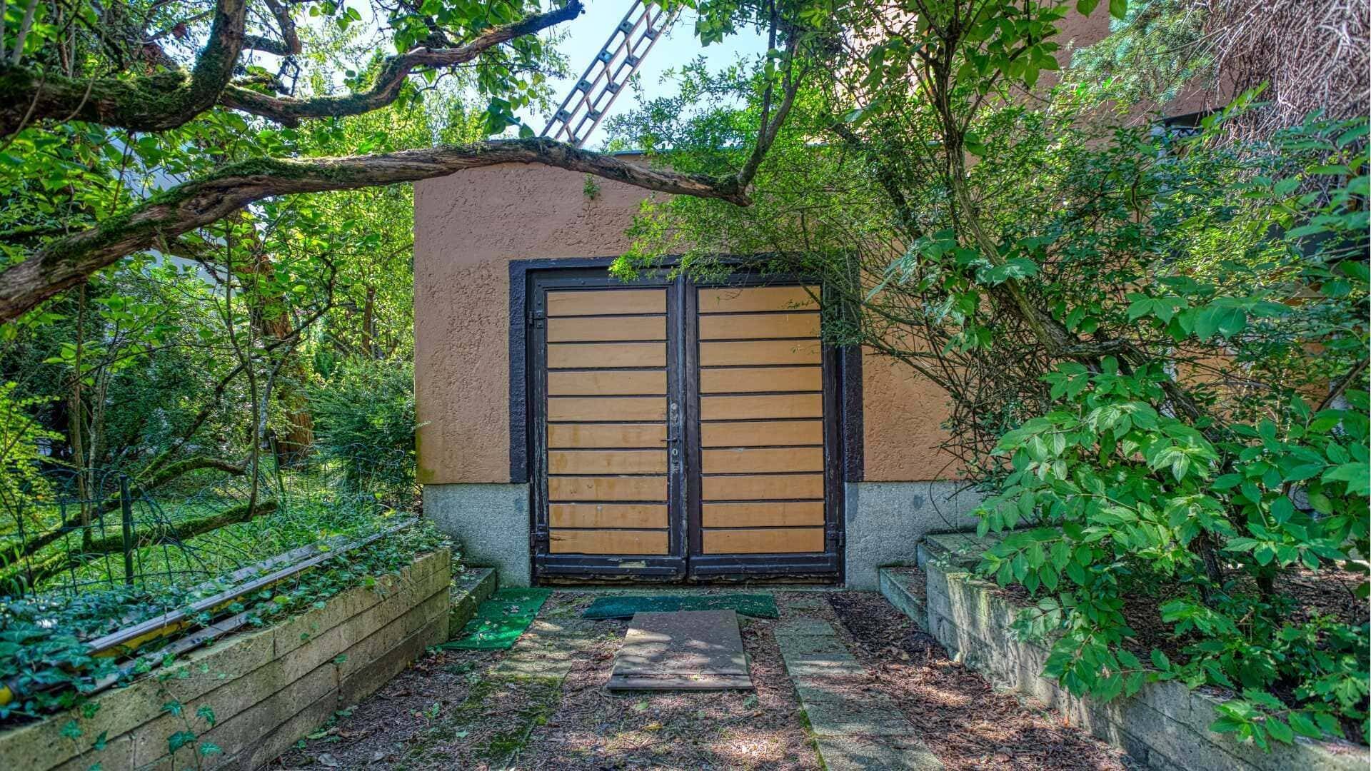 Wooden garage door surrounded by dense vegetation on the property in Munich-Laim