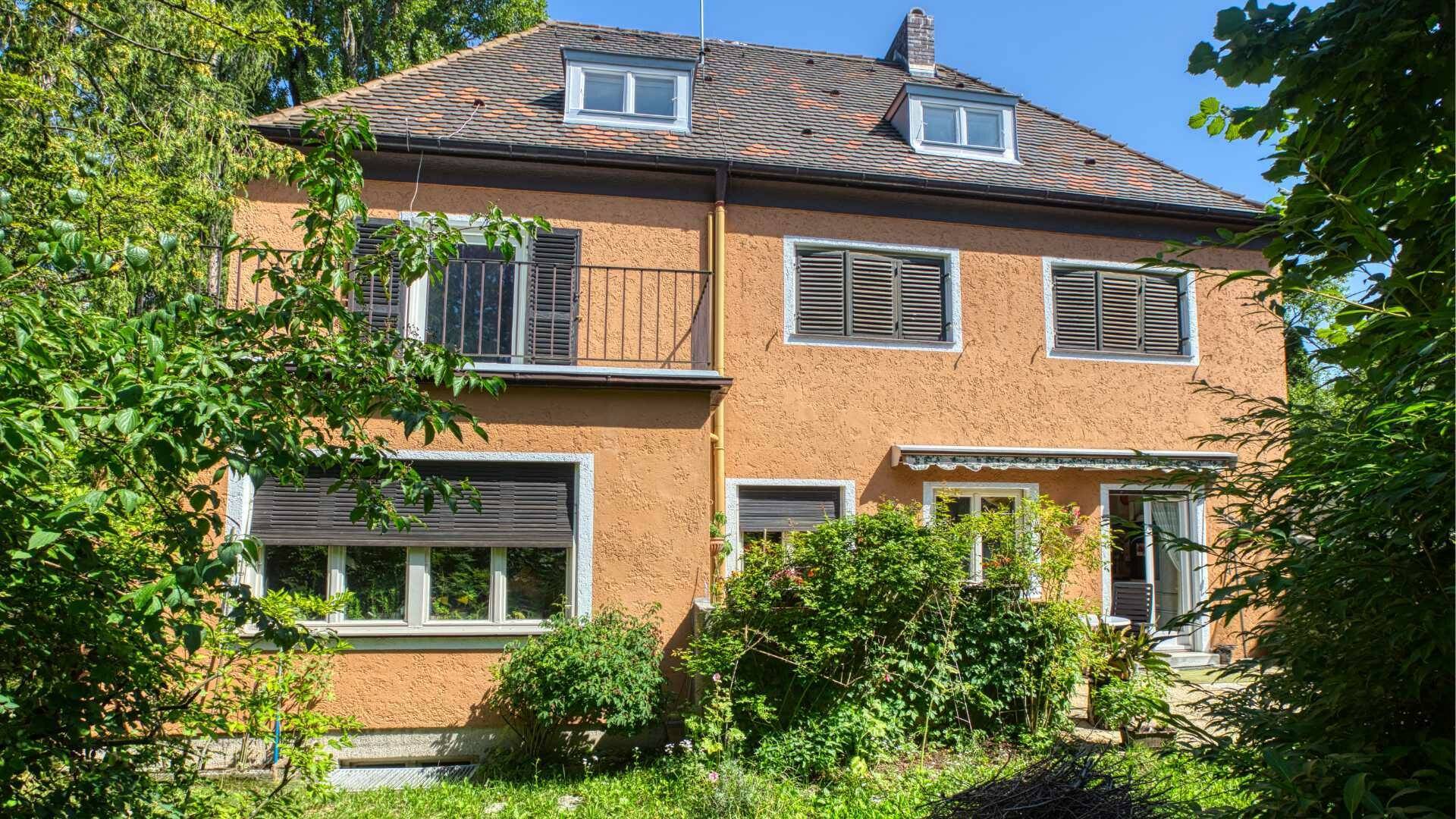 Two-family house in Laim with an ochre-colored facade, shutters, balcony, and a landscaped front garden.