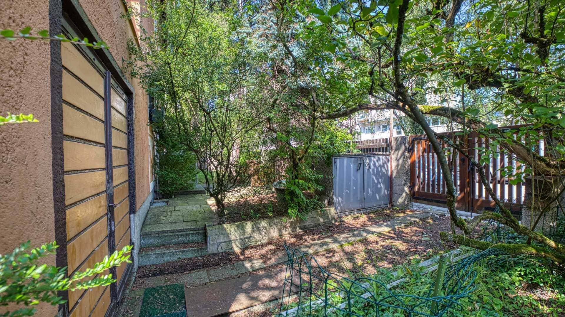 Shady garden path with a wooden fence and dense vegetation on the property in Munich-Laim