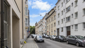 Narrow street with parked cars between bright residential buildings in Munich-Lehel