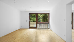 Empty living room with window, balcony door, and green view in rental apartment Munich-Lehel