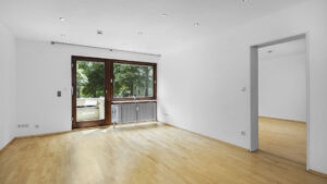 Empty living room with dark balcony door, wooden floor, and doorway to another room in a rented apartment in Munich-Lehel