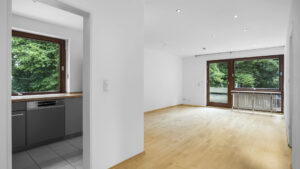 Empty living room with hardwood floor, patio door, and view through to the kitchen in a rental apartment in Munich-Lehel