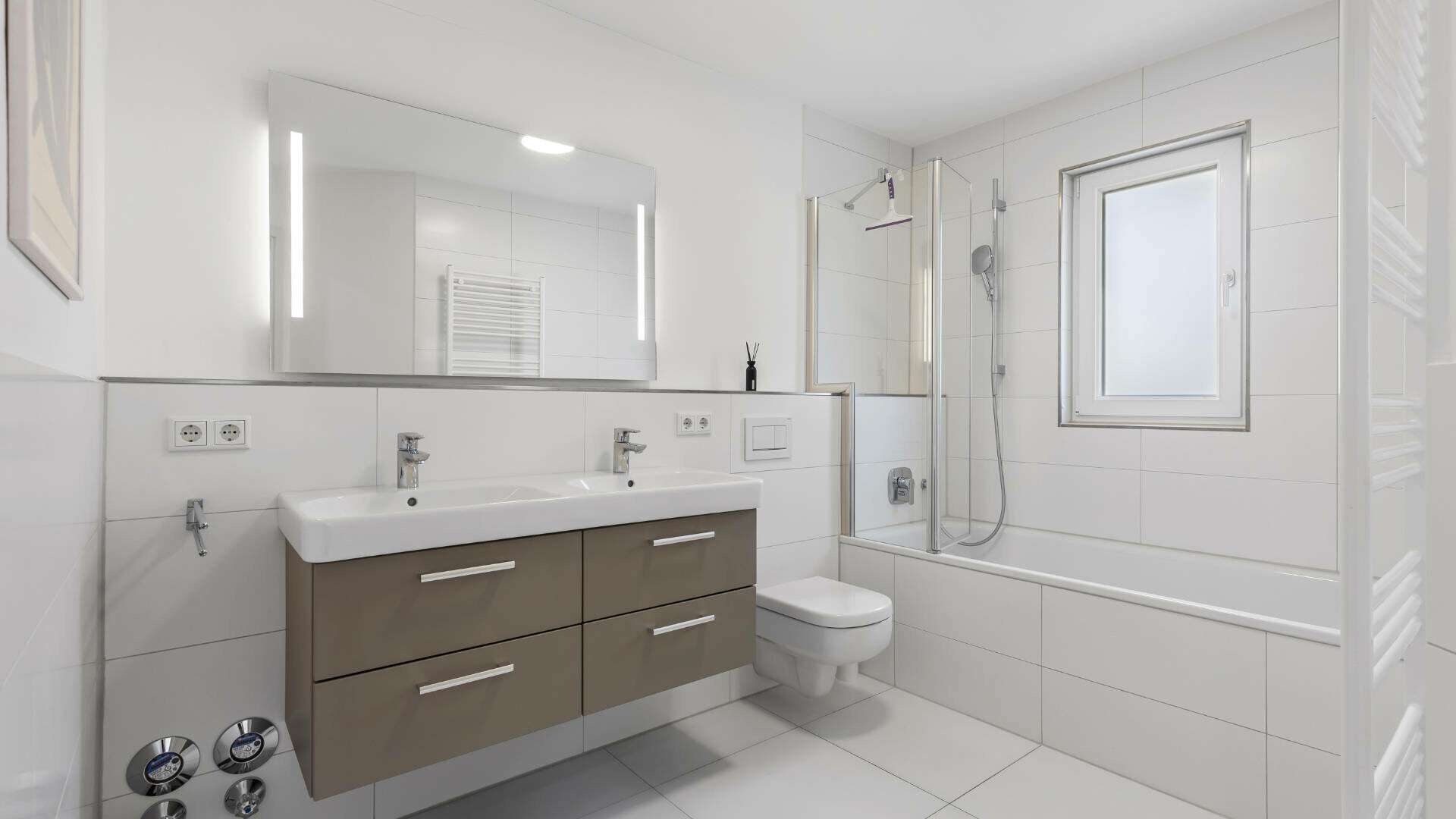 Modern bathroom in Lerchenau with double vanity, bathtub, and illuminated mirror.